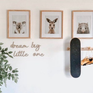 May include: Three framed animal prints featuring a koala, kangaroo, and wombat. The frames are light wood and have a white mount. The prints are on a white wall with a skateboard and a pair of shoes hanging below. The text "dream big little one" is written in cursive on the wall.