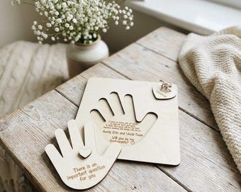 May include: Wooden hand-shaped plaques with engraved text. One plaque has a cutout handprint, the other has a smaller hand shape with a heart. Text includes "There is an important question for you" and "Will you be my Godparents?"