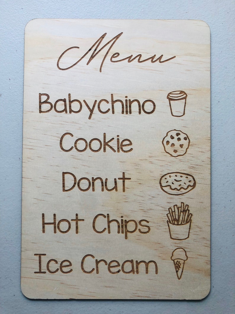Puede incluir: Una tabla de men&uacute; de madera con esquinas redondeadas. La palabra "Menu" est&aacute; en la parte superior en cursiva. Debajo est&aacute;n las palabras "Babychino", "Cookie", "Donut", "Hot Chips" e "Ice Cream", cada una con una ilustraci&oacute;n correspondiente.