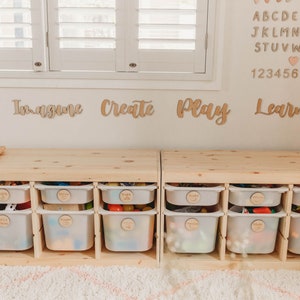 May include: Two wooden storage units with white plastic drawers, each labeled with a different word. The words are "Imagine", "Create", "Play", and "Learn". The units are sitting on a light brown rug.