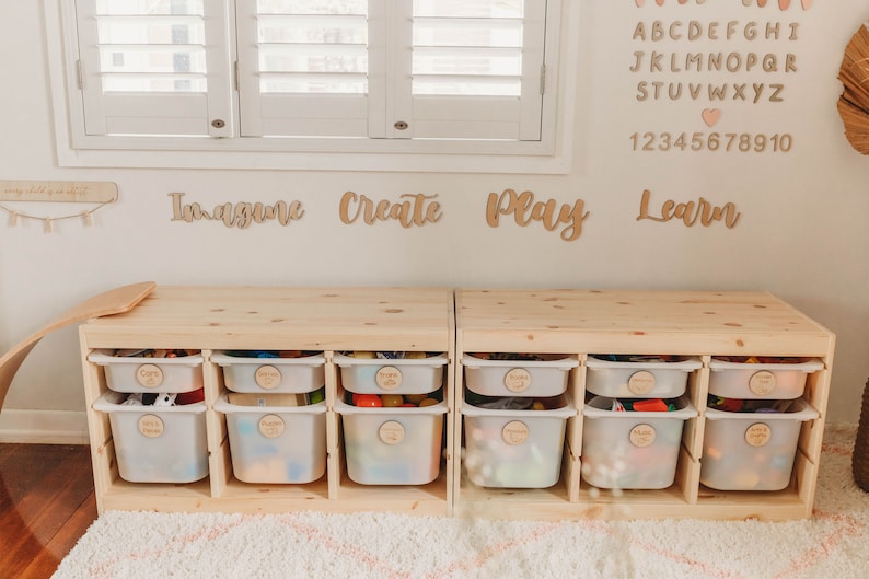 May include: Two wooden storage units with white plastic drawers, each labeled with a different word. The words are "Imagine", "Create", "Play", and "Learn". The units are sitting on a light brown rug.