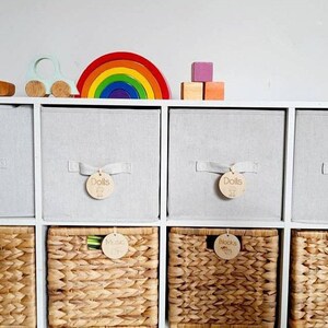 May include: White cube storage shelves with woven baskets labeled "Dolls", "Blocks", and "Music". The shelves are decorated with a rainbow arch, a toy car, and wooden blocks.