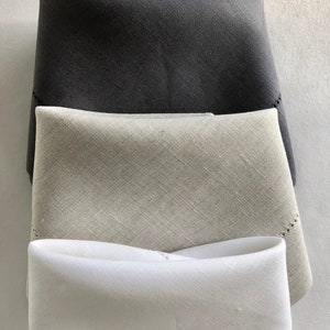 May include: Three linen napkins in different shades of gray, white, and black. The napkins are folded and stacked on top of each other.