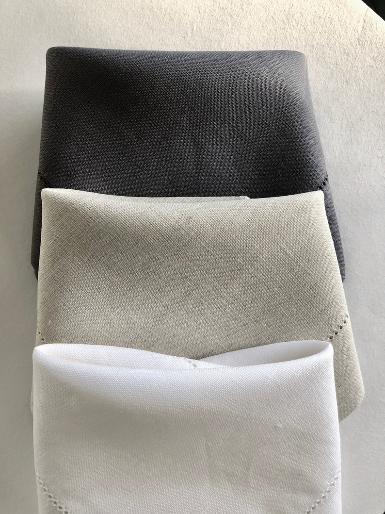 May include: Three linen napkins in different shades of gray, white, and black. The napkins are folded and stacked on top of each other.