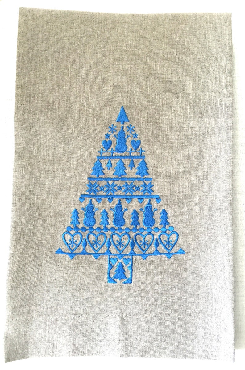 May include: A blue embroidered Christmas tree design on a linen kitchen towel. The tree is decorated with snowflakes, hearts, and snowmen.