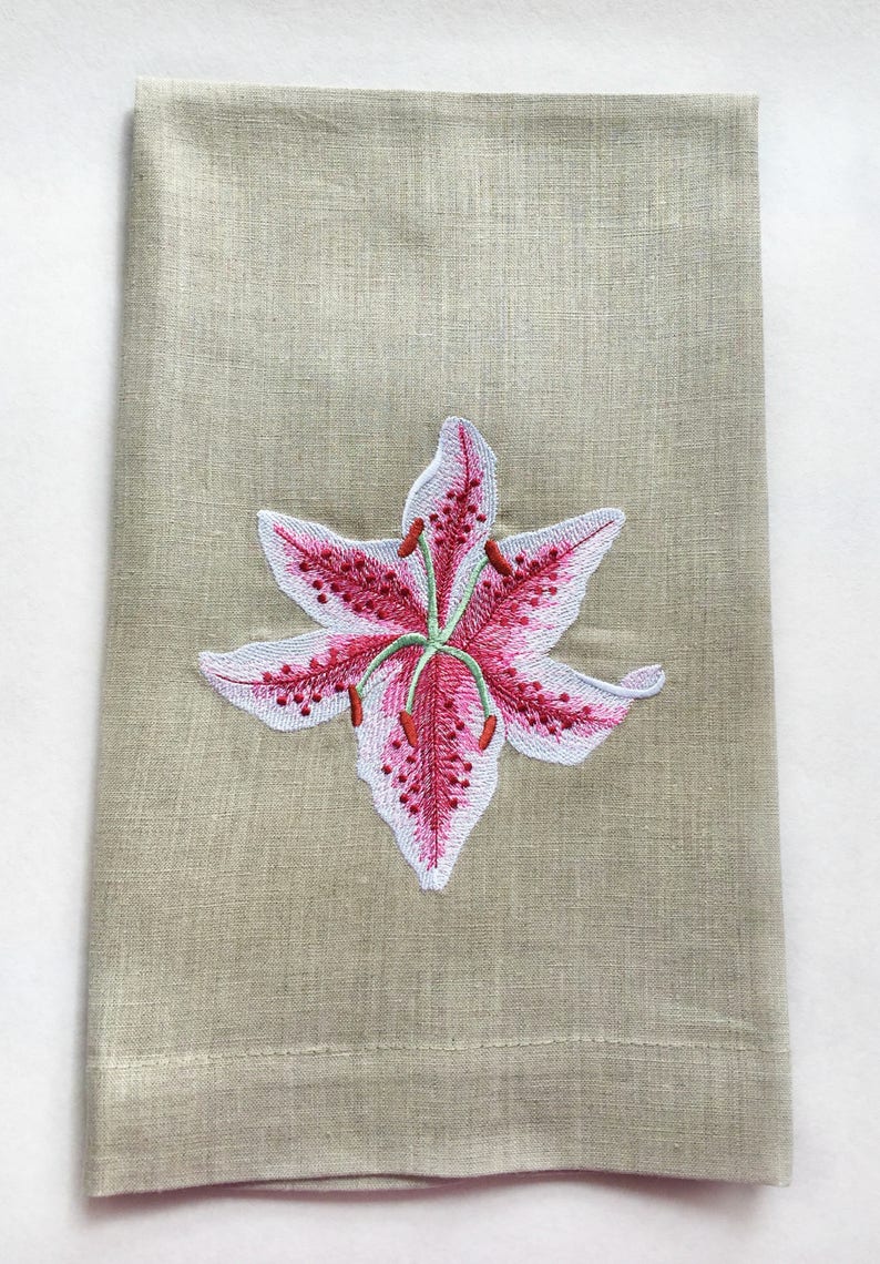 Pu&ograve; includere: Un asciugamano da cucina in lino beige con un ricamo di giglio rosa e bianco.