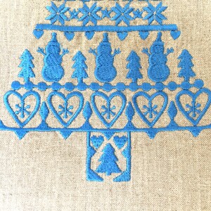 May include: Blue embroidered Christmas tree design on a beige linen fabric. The tree is decorated with snowmen, hearts, and snowflakes.
