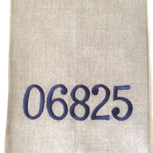 May include: A beige linen kitchen towel with the number 06825 embroidered in dark blue thread.