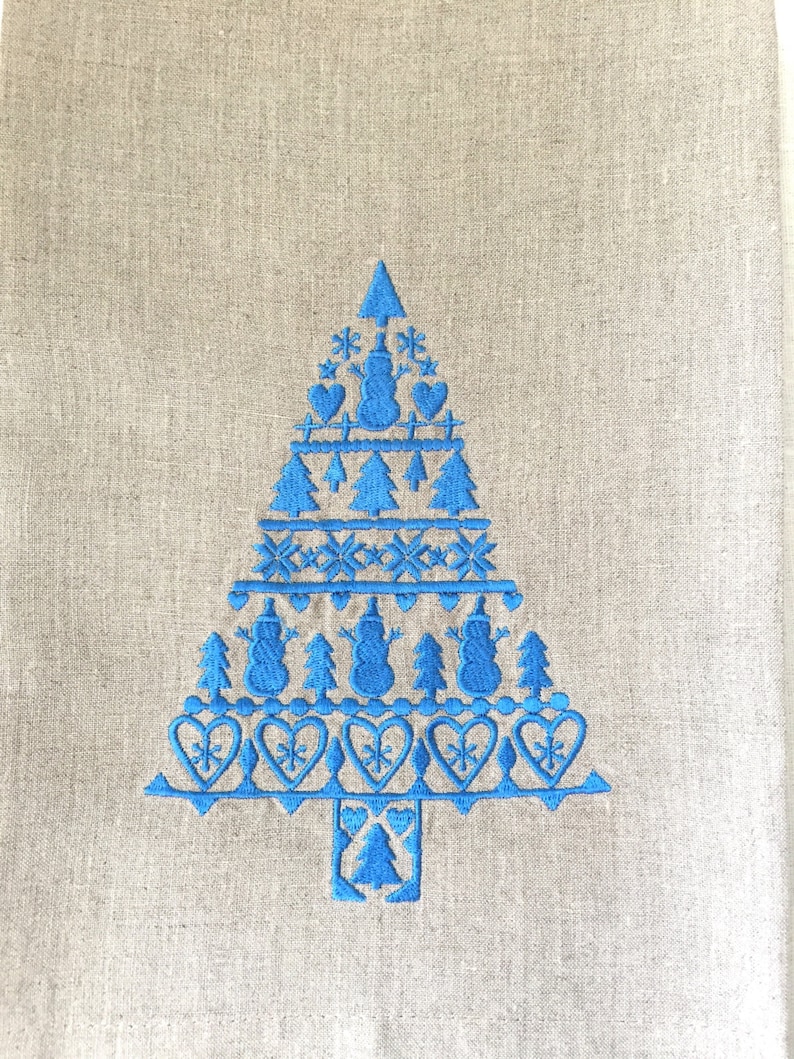 May include: A blue embroidered Christmas tree design on a beige linen kitchen towel. The design features a tree with a star on top, snowmen, hearts, and snowflakes.