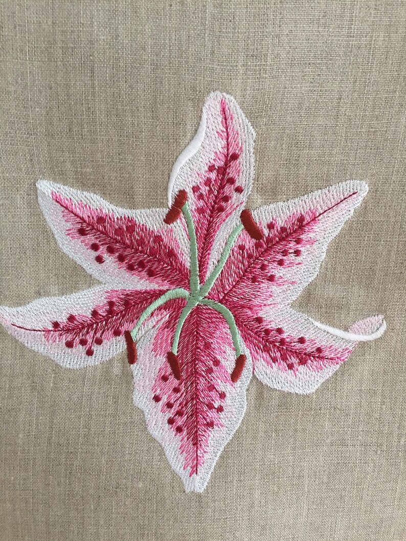 Pu&ograve; includere: Fiore di giglio ricamato rosa e bianco su uno sfondo di tessuto di lino beige.