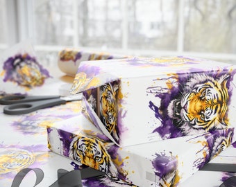 May include: Two gift boxes wrapped in white paper with a watercolor design of a tiger with purple and yellow accents. The boxes are stacked on top of each other and are sitting on a table covered in the same wrapping paper.