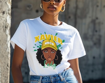 May include: White t-shirt with a graphic of a woman wearing a yellow cap with the text "HBCU" on it. The text "XAVIER Lady" is printed on the shirt.