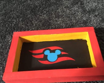 May include: A small wooden box with a red, yellow, and black painted design. The box features a blue Mickey Mouse head with red and white waves.