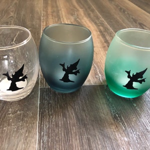 May include: Three glass candle holders with a gradient color effect. The holders are clear, blue, and green. Each holder has a black silhouette of a tree with a bird on a branch.