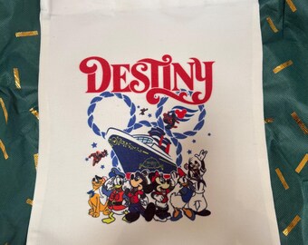 May include: Cream-coloured tote bag with the word "Destiny" in red and blue lettering. The bag features a graphic of a cruise ship and cartoon characters including Mickey Mouse, Minnie Mouse, Donald Duck, and Goofy.