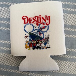 Pode incluir: Isolador de bebidas branco com a palavra "Destiny" em escrita vermelha acima de um gráfico de navio de cruzeiro com Mickey Mouse e seus amigos. O design inclui detalhes de corda azul e personagens de desenhos animados.