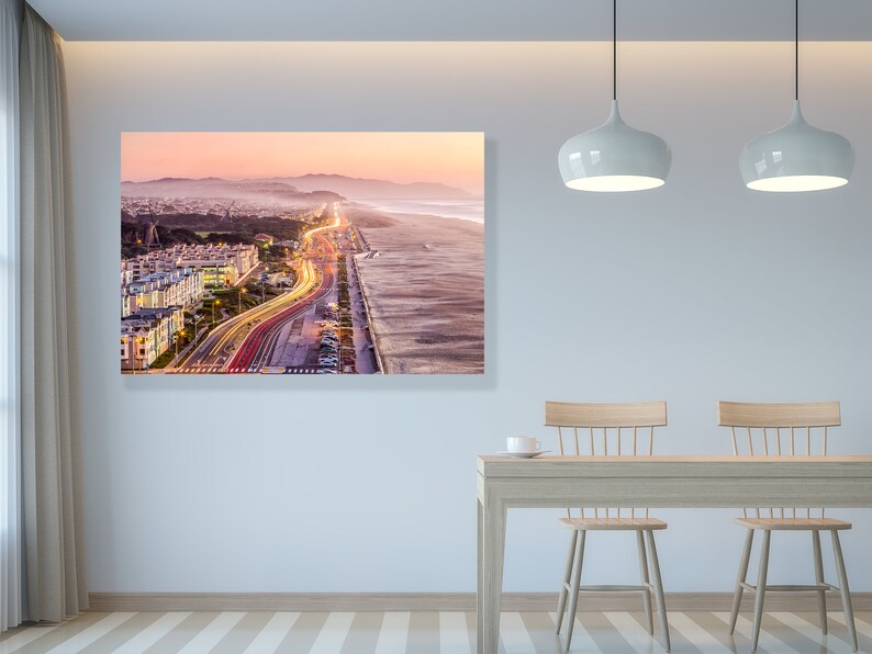 May include: An aerial view of a city at sunset with a highway leading to the beach. The highway is lined with streetlights and the beach is sandy with waves crashing on the shore.
