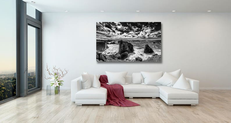 May include: Black and white photograph of a rocky coastline with crashing waves and a dramatic cloudy sky.