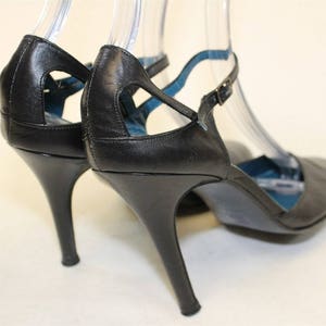 May include: A pair of black leather heeled shoes with ankle straps. The shoes have a cut-out design on the vamp and a blue lining.