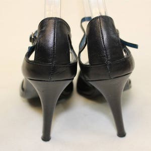May include: A pair of black leather heeled sandals with ankle straps. The straps have a blue trim.