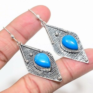 May include: Silver dangle earrings with a blue turquoise stone set in a diamond-shaped frame.