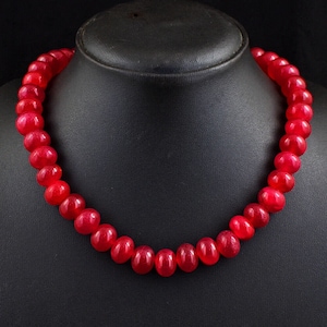 Könnte beinhalten: Eine Halskette aus roten Edelsteinperlen mit runden Perlen. Die Halskette wird auf einem schwarzen Samtständer präsentiert.