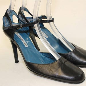 May include: A pair of black leather heeled shoes with ankle straps. The shoes have a blue insole and the brand name "Charles David" is printed on the insole.