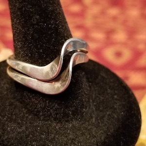May include: A silver ring with a wavy design. The ring is made of two bands that are intertwined.