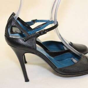 May include: Black leather heeled shoes with a blue lining and a buckle strap.
