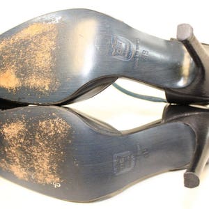 May include: A pair of black leather heeled shoes with a strap across the top of the foot. The shoes have a worn look and the soles are visible.