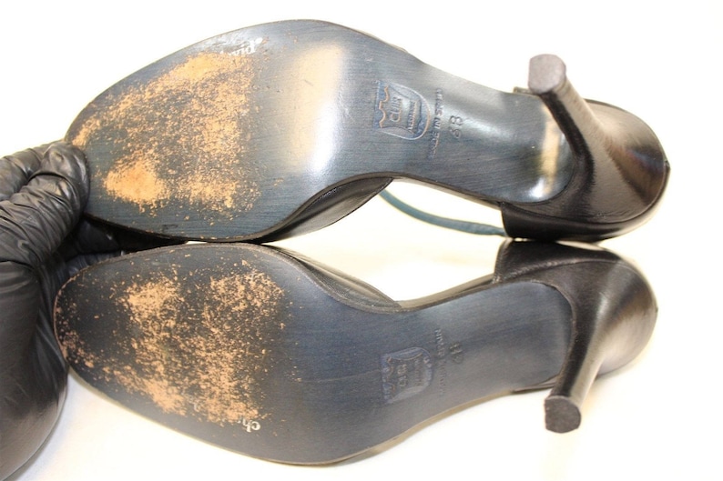 May include: A pair of black leather heeled shoes with a strap across the top of the foot. The shoes have a worn look and the soles are visible.