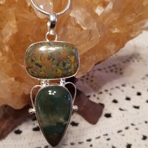May include: A silver pendant with two green and brown stones. The top stone is rectangular and the bottom stone is teardrop shaped.