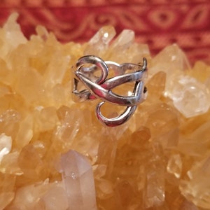 May include: A silver ring with a delicate, intricate design. The ring is made of a single piece of metal that is twisted and turned to create a unique and eye-catching pattern.