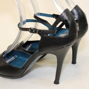 May include: Black leather heeled shoes with ankle straps and a blue lining. The shoes have a stiletto heel.