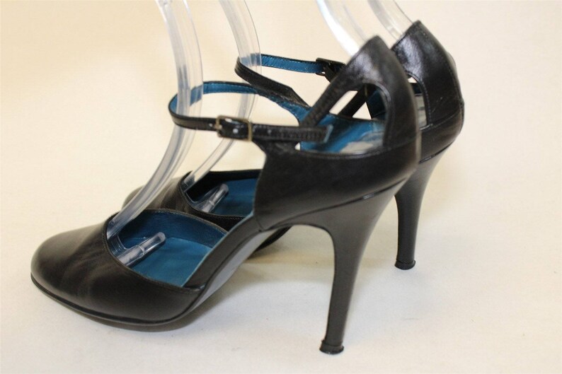 May include: Black leather heeled shoes with ankle straps and a blue lining. The shoes have a stiletto heel.