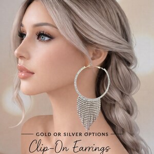 Könnte beinhalten: Große, silberfarbene Clip-Ohrringe mit einem Reifen-Design und baumelnden Kristallfransen. Die Ohrringe werden an einer Person mit blondem Haar gezeigt. Der Text "GOLD OR SILVER OPTIONS" und "Clip-On Earrings" ist ebenfalls sichtbar.