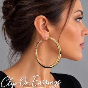 Op de afbeelding: Grote, gepolijste goudkleurige oorringen met een glad, afgerond oppervlak. Deze ronde oorbellen zijn voorzien van een clipmechanisme voor bevestiging aan de oorlel. De tekst "Clip-On Earrings" staat in witte letters onderaan de afbeelding.