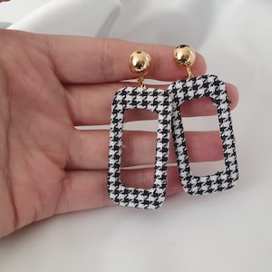 May include: A pair of black and white houndstooth patterned earrings with gold-toned metal accents.