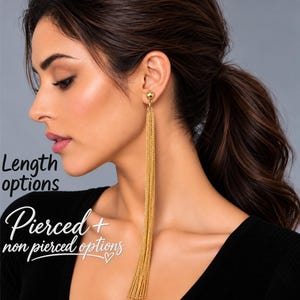 Può includere: Un lungo orecchino a nappa color oro con un piccolo perno sferico collegato a diverse delicate catenelle pendenti. L'immagine include il testo Length options e Pierced + non pierced options.