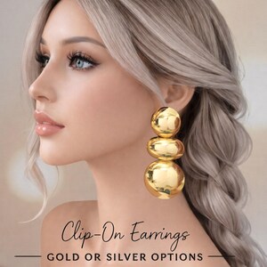 May include: Gold clip-on earrings with a three-sphere design. The earrings are shown on a person with blonde hair. The text "Clip-On Earrings" and "GOLD OR SILVER OPTIONS" is also visible.
