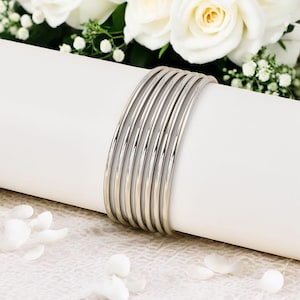 May include: A stack of silver bangles, arranged in a circle, on a white surface.