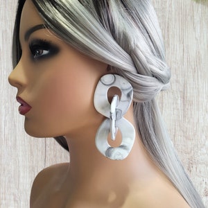 May include: A pair of large, white and gray marble-patterned statement earrings. The earrings are made of two interlocking circles.