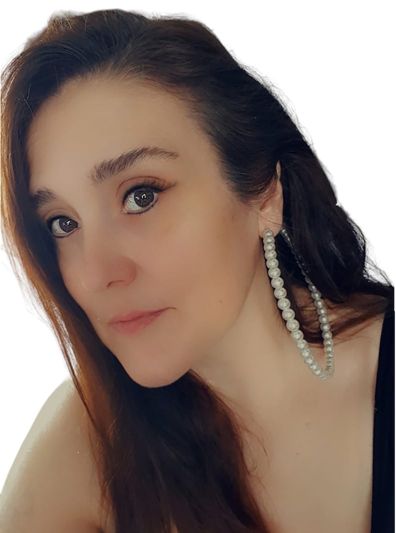 Pu&ograve; includere: Primo piano di una persona che indossa grandi orecchini a cerchio. Gli orecchini sono adornati con molteplici piccole perle bianche rotonde. La persona ha i capelli castani e guarda verso sinistra. Lo sfondo &egrave; bianco.
