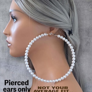 Pu&ograve; includere: Una persona con i capelli grigi indossa un grande orecchino a cerchio di perle. L'orecchino &egrave; fatto di perle bianche e ha una chiusura argentata. Il testo sull'immagine recita: "Pierced ears only. Not your average fit... I'm larger! Check my size so there are no surprises."