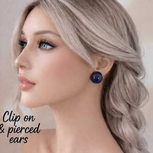 Może przedstawiać: Profil osoby z jasnymi blond włosami i niebieskimi oczami, noszącej ciemnoniebieskie, okrągłe kolczyki. Obraz zawiera tekst "Clip on & pierced ears" w czcionce pisanej odręcznie.