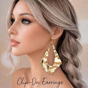 Op de afbeelding: Goudkleurige clip-on oorbellen met een gehamerde textuur. De oorbellen hebben een ruitvorm met een open midden. De tekst "Clip-On Earrings" staat cursief onderaan de afbeelding.
