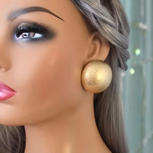 May include: A pair of gold-toned round clip-on earrings. The earrings have a textured surface.