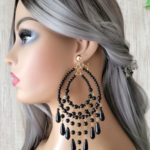 May include: Large black dangle earrings with gold accents. The earrings are made of black beads and have a teardrop shape.