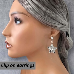 May include: Silver-toned clip-on earrings featuring a dangling star design. The star-shaped earrings are embellished with clear rhinestones. The image includes the text "Clip on earrings".
