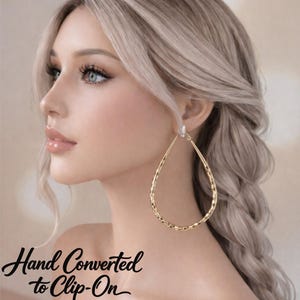 May include: Gold teardrop earrings with a textured surface. The earrings are clip-on style, as indicated by the text "Hand Converted to Clip-On". The earrings are a bright gold color and are a statement piece.